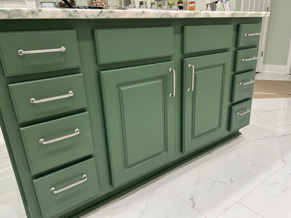 Green kitchen island with marble countertop and silver hardware, featuring multiple cabinets and drawers.
