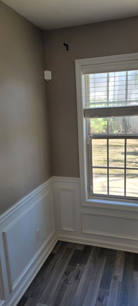 Interior corner of a room featuring a window, gray walls, and wood flooring.