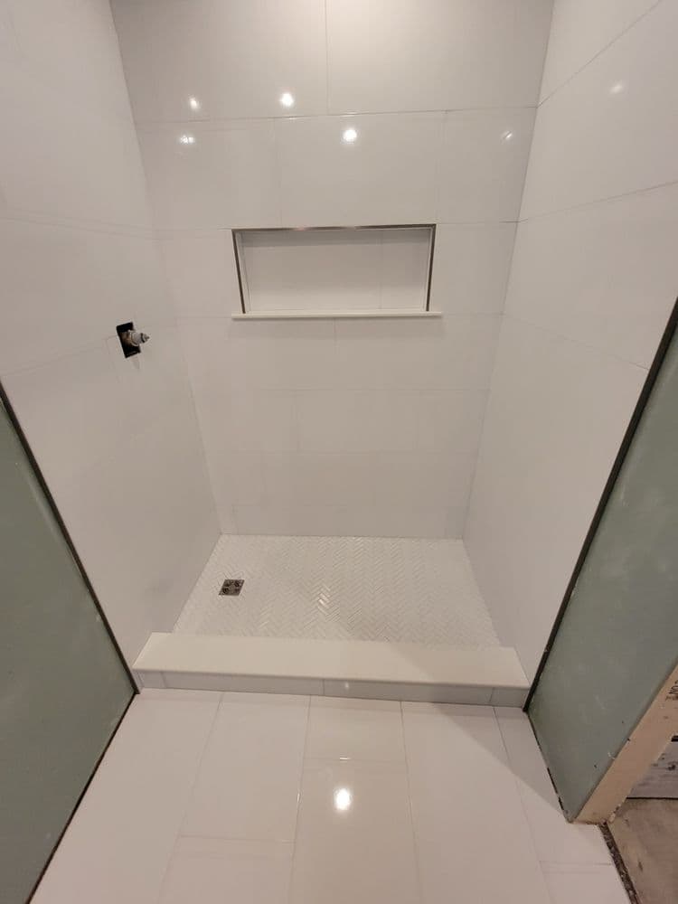 Modern shower space with white tile walls, floor, and built-in shelf for toiletries.