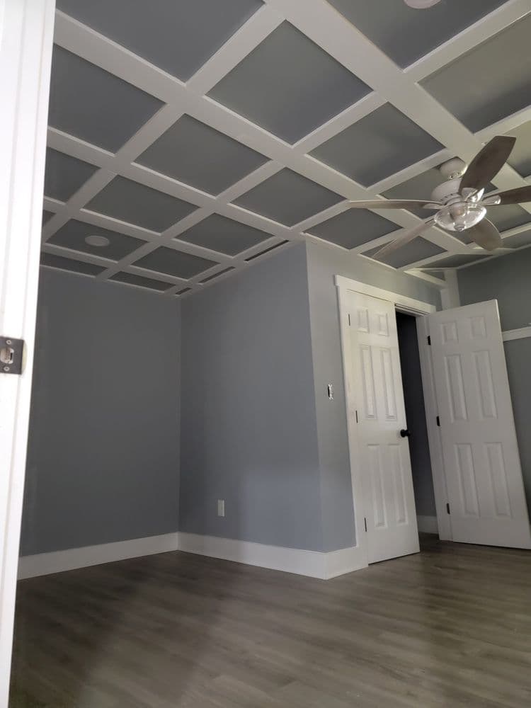 Modern interior room with gray walls, a coffered ceiling, and a stylish ceiling fan.