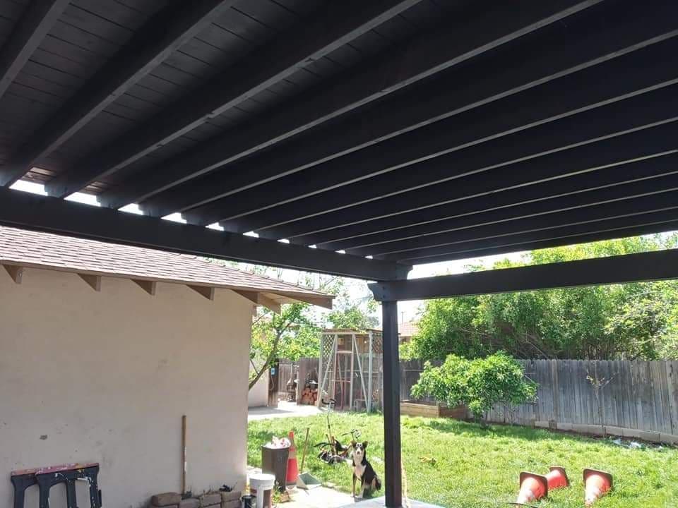 View of a modern patio structure with beams, grass yard, and tools in the background.