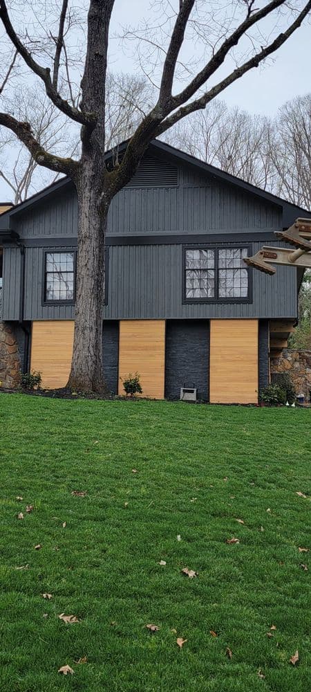 Modern two-story house with wooden garage doors and a large tree in the front yard.