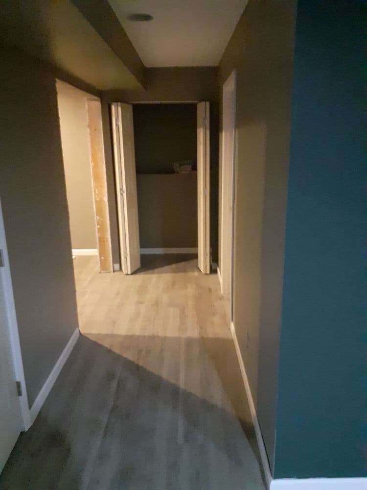 Empty hallway with open doors, wooden flooring, and neutral wall colors. Bright lighting highlights space.