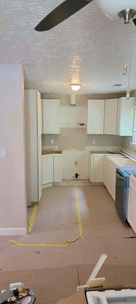 Renovated kitchen with white cabinets, unfinished walls, and new appliances in progress.
