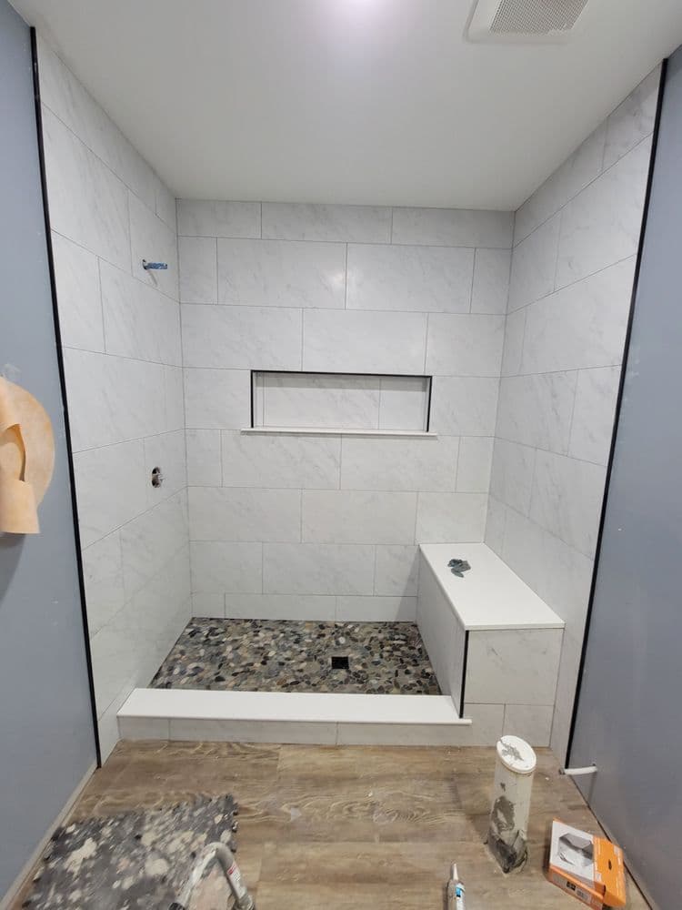 Modern bathroom under renovation with marble tiles, shower niche, and stone floor.