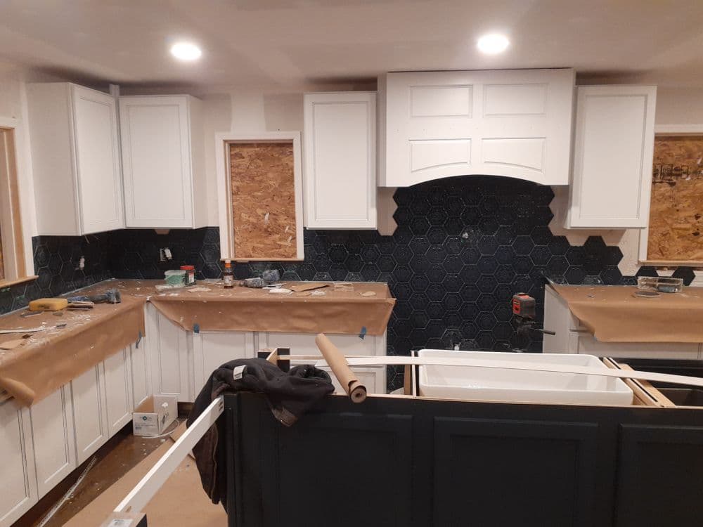 Renovated kitchen with white cabinets, black hexagon backsplash, and construction materials visible.