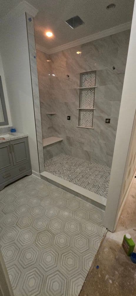 Modern bathroom with gray tiled shower, geometric floor, and sleek vanity cabinets.