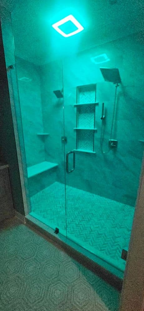 Modern glass shower with teal lighting, herringbone tile flooring, and sleek fixtures.