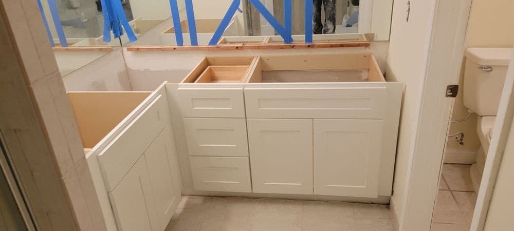 Bathroom renovation featuring white cabinetry, unfinished sink area, and construction tape.