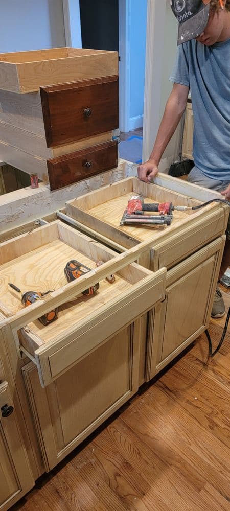 Person working on custom kitchen cabinetry, featuring empty drawers and tools on a wooden countertop.