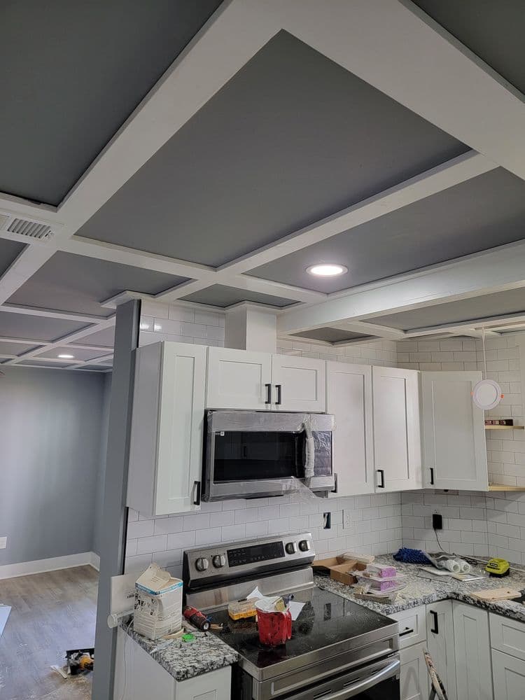 Modern kitchen featuring gray coffered ceiling, white cabinets, and stainless steel appliances.