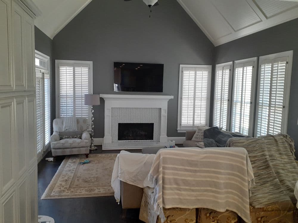Cozy living room with gray walls, white fireplace, and large windows. Elegant furniture and decor.