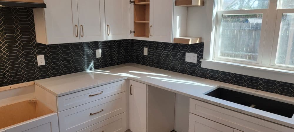 Modern kitchen with white cabinets, black geometric backsplash, and minimalist design.