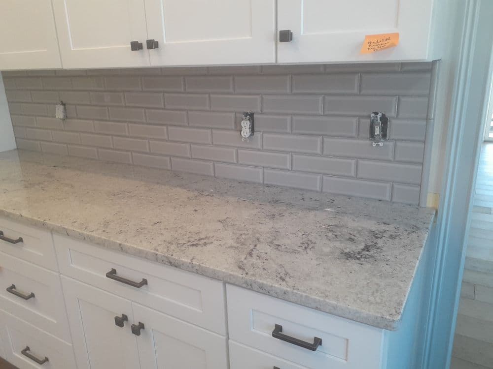Modern kitchen counter with gray backsplash, white cabinets, and granite surface.